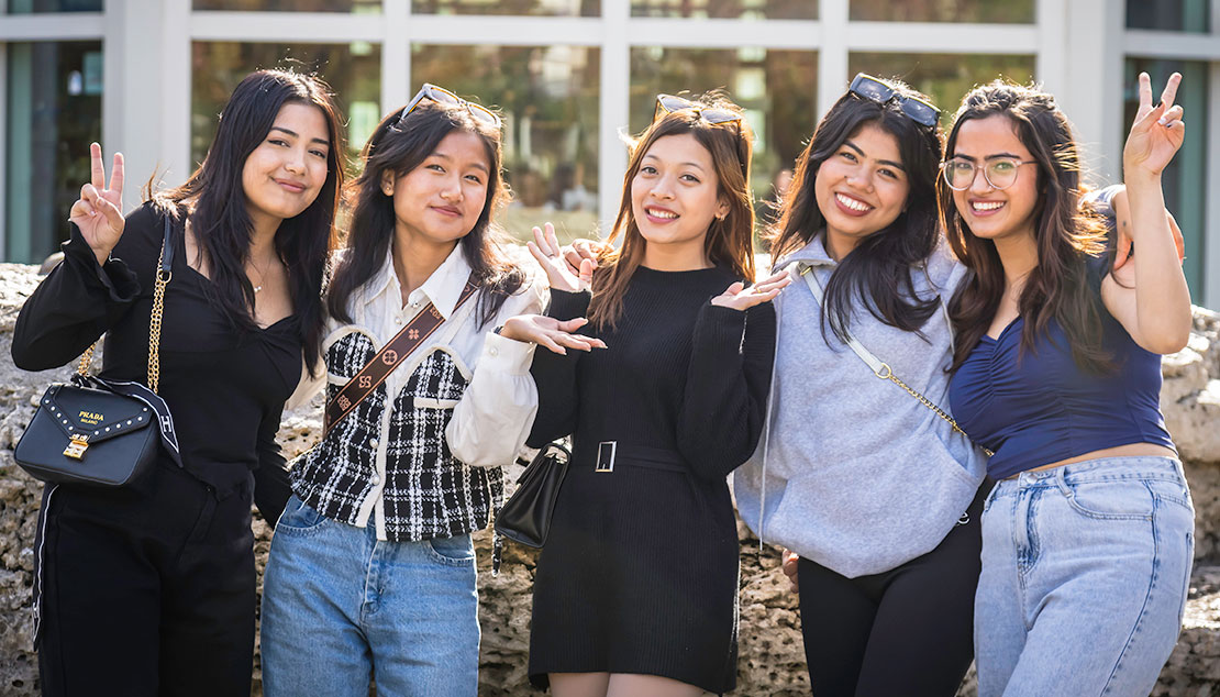 Five students smiling at the camera outside of a building on campus in St. Louis.