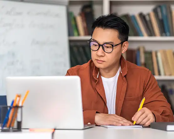 Adult student looking toward a laptop, while writing on a notepad.