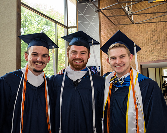 Three graduates in cap and gowns with cords