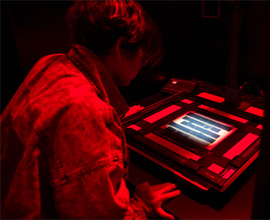 Student working under red light looking at 35mm film strips on a light box