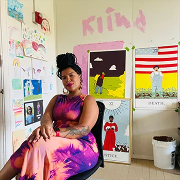 Simiya Sudduth sits in their studio, surrounded by colorful art.