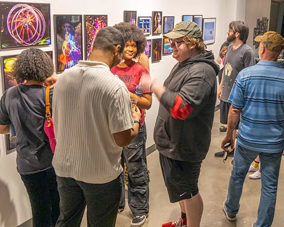 Gallery walls with photos and large group of people looking and talking