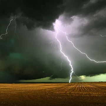 A lightning bolt forks from a dark cloud and hits a golden field, green sky in the distance.