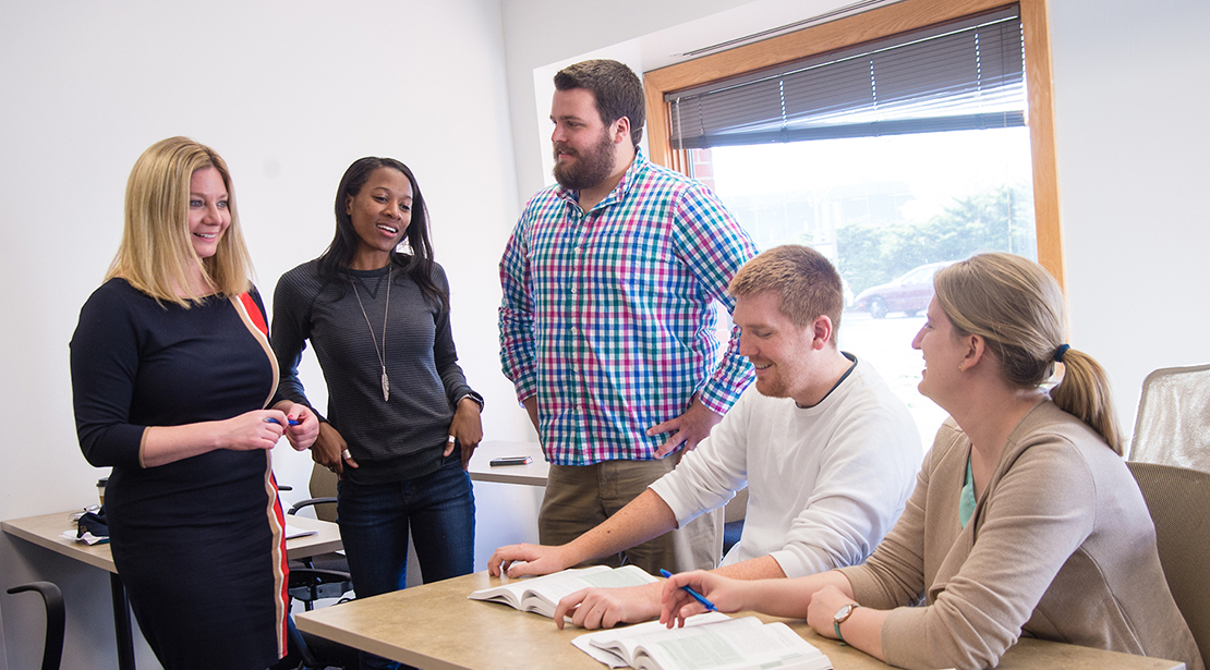 Several students sitting and standing, having a discussion in a classroom.