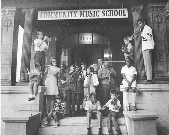 children holding instruments on porch below sign reading Community Music School