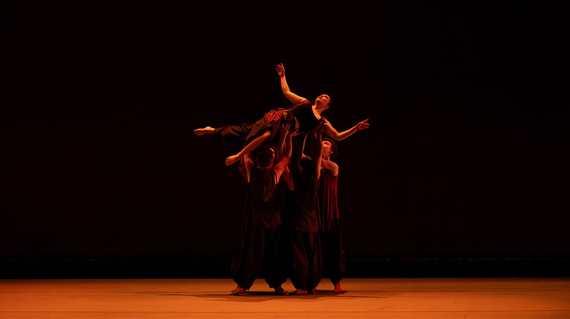 Dances bathed in orange light against a dark backdrop.
