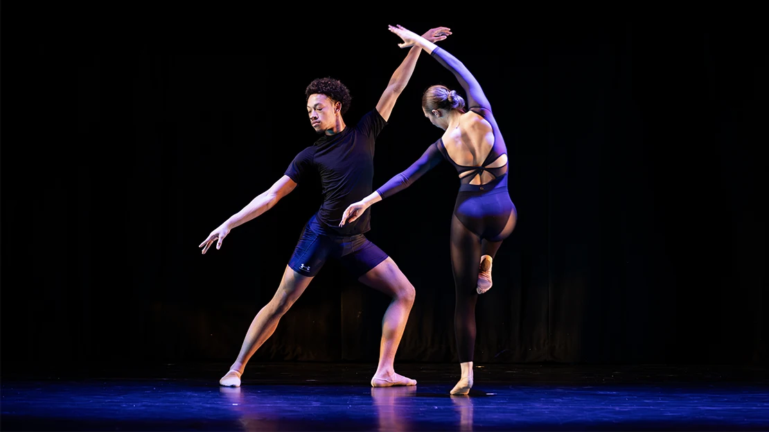 Two dancers in simple costumes perform under blue light.