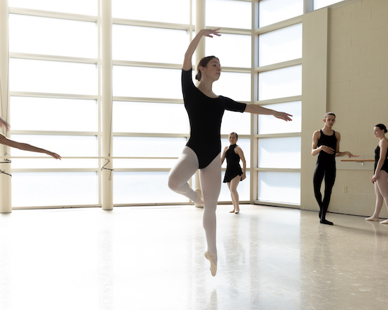 Students in a dance studio practicing at a ballet barre.