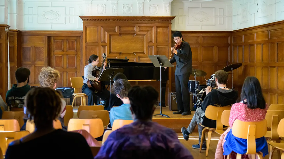 Students perform on guitar and violin in front of an audience.