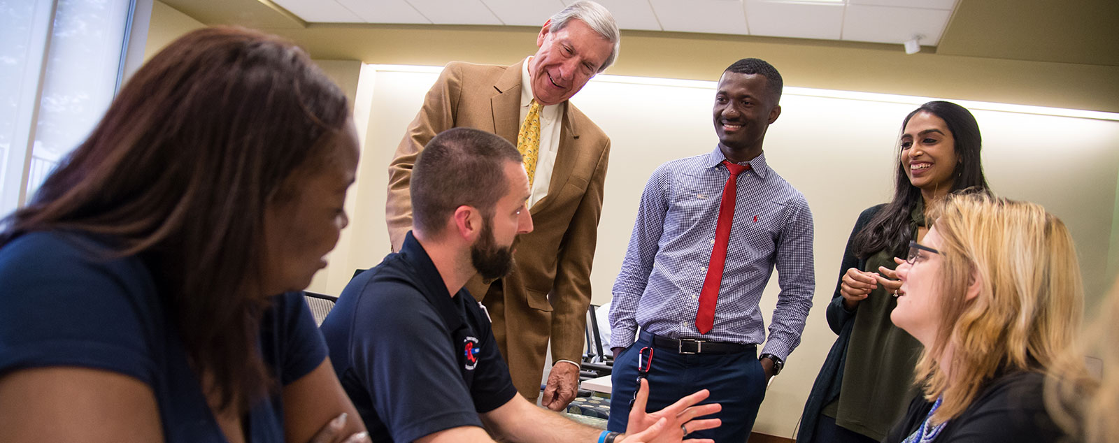 Group of students sit around table and talk with professor
