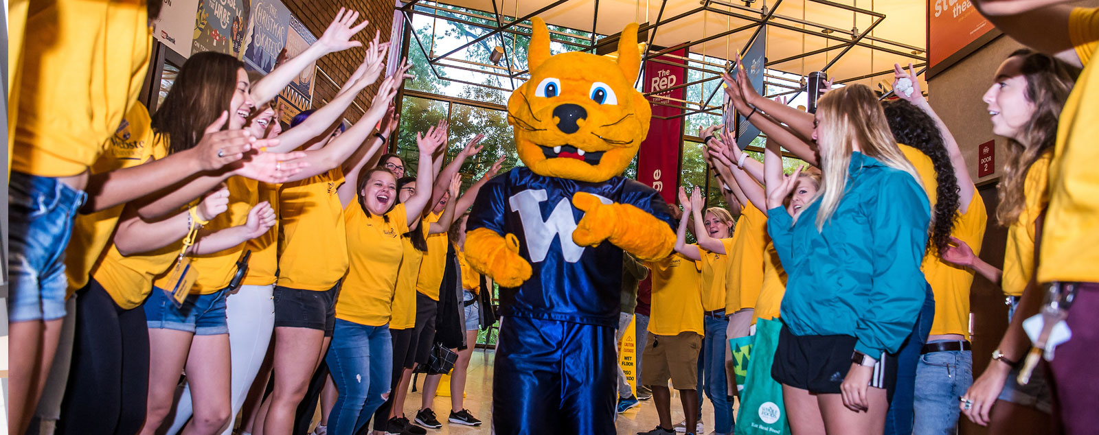 Gorlok mascot runs through a crowd of Webster students wearing yellow shirts and cheering it on.