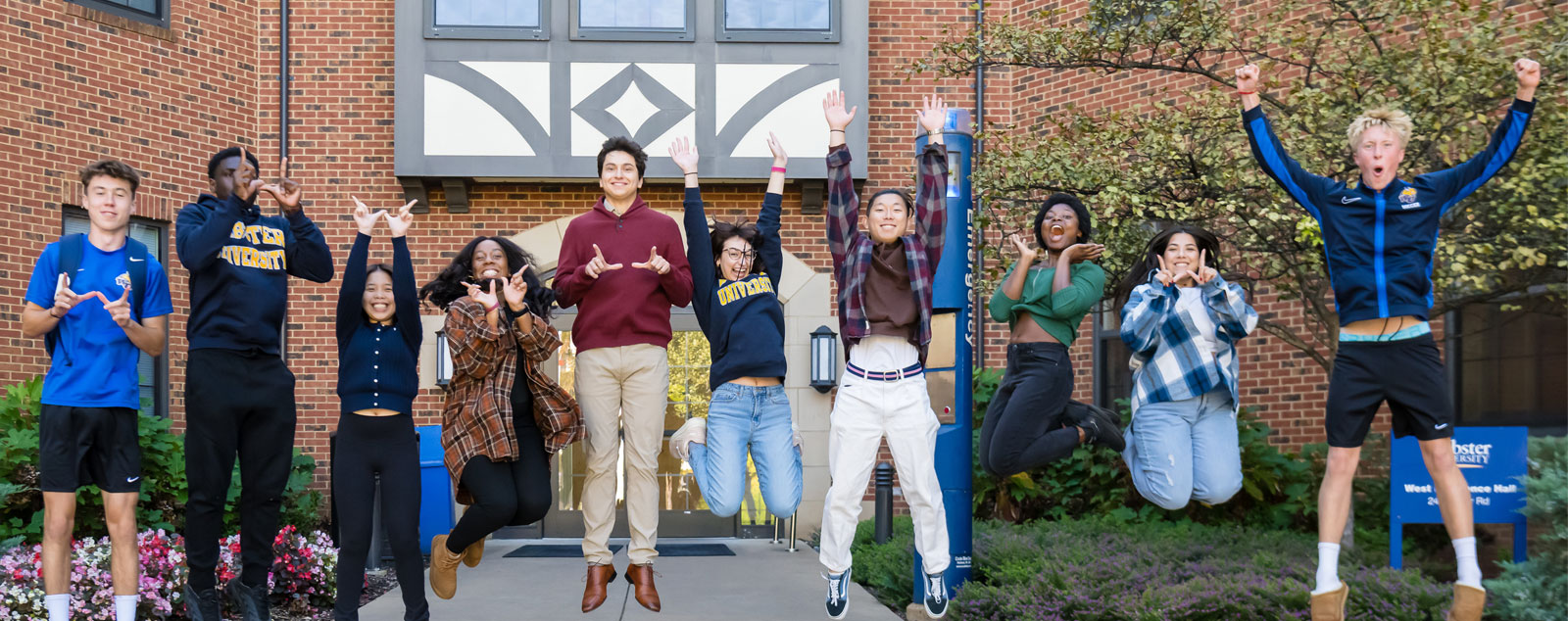 Group of Webster students standing in a line in front of residence hall smiling and waving