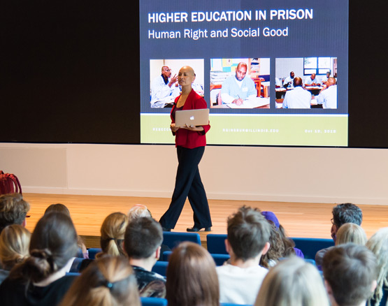 Speaker walks in front of screen that reads "Higher Education in Prison: Human Right and Social Good"