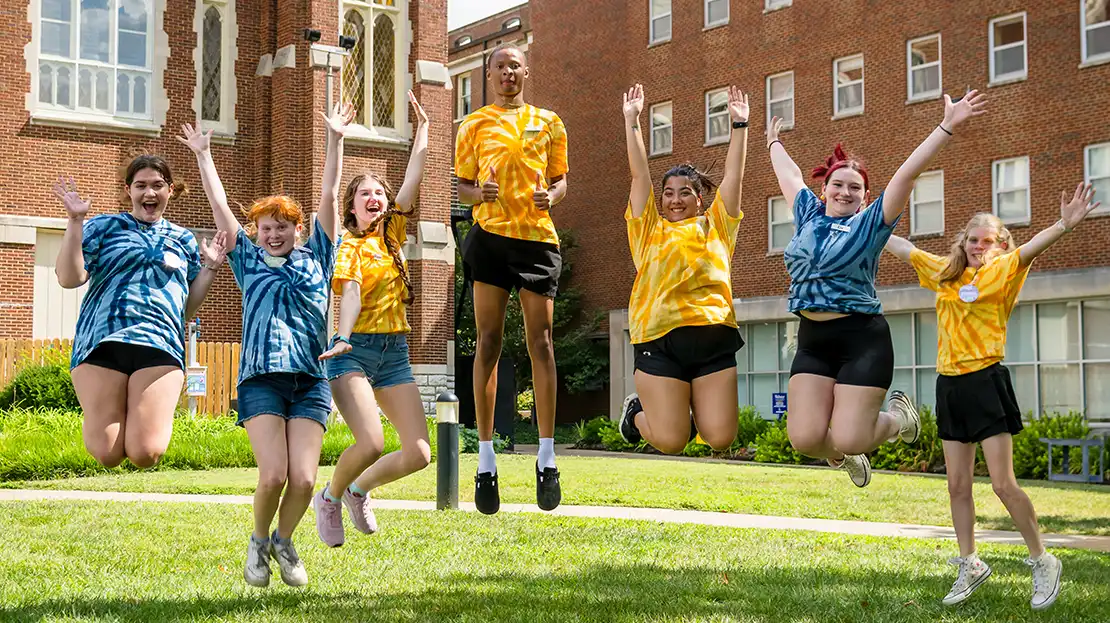 Group of undergraduate students smiling and jumping in the air in matching T-shirts