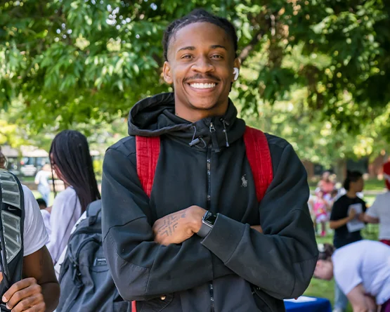Student with backpack standing on campus, smiling.