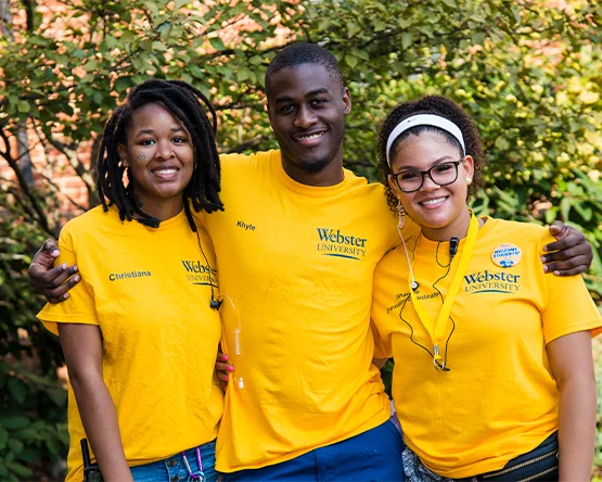 Three students in matching yellow T-shirts, arms around each other's shoulders, smiling.