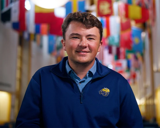 A student poses for a photo in the UC where there are many different flags from across the world displayed.