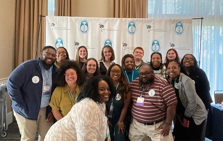 Webster University professional counseling students gather in front of an SCCA step and repeat at the conference for a photo.